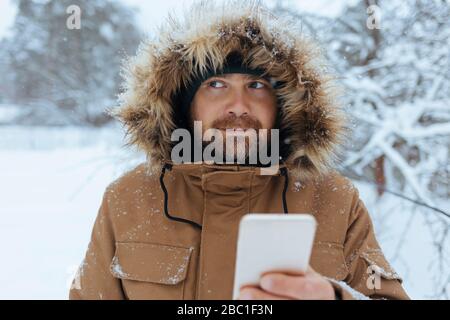 Portrait de l'homme pensif avec téléphone cellulaire en hiver Banque D'Images