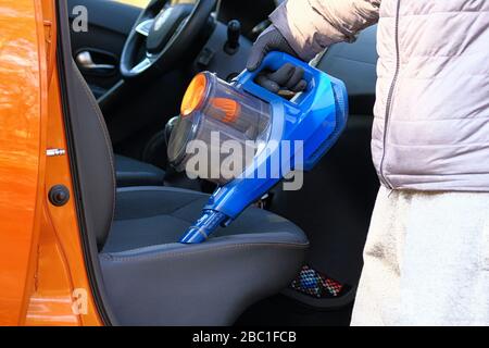 Aspirateur entre les mains du conducteur. Nettoyage de l'intérieur de l'automobile avec aspirateur bleu, fermeture. Les sièges en textile de voiture sont régulièrement dépollution. Horizon Banque D'Images