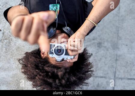 Jeune homme posé sur le mur et prenant des photos avec son appareil photo et pointant avec son doigt Banque D'Images