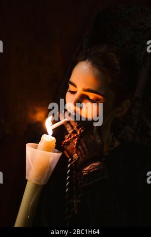 Belle femme composée en costume traditionnel pour la semana santa, éclairage de cigarette sur bougie brûlante Banque D'Images