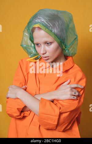 Portrait de la jeune femme avec sac en plastique sur sa tête portant une veste orange devant un fond jaune Banque D'Images