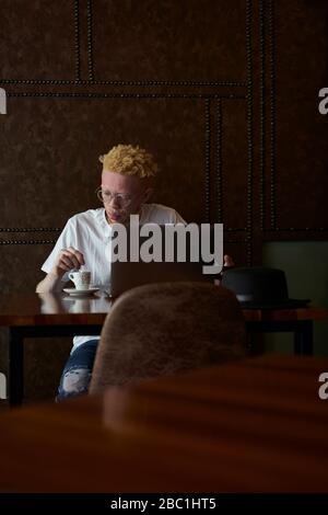 Albino homme ayant un café et travaillant sur son ordinateur dans une cafétéria Banque D'Images