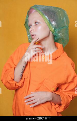 Portrait de la jeune femme avec sac en plastique sur sa tête portant une veste orange devant un fond jaune Banque D'Images