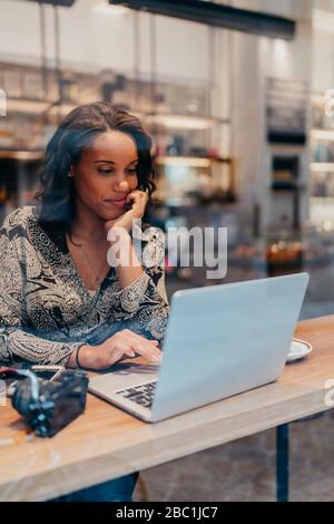 Jeune femme avec un appareil photo utilisant un ordinateur portable dans un café derrière le panneau de fenêtre Banque D'Images