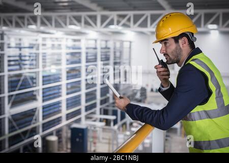 Superviseur masculin avec tablette numérique parlant, utilisant la plate-forme walkie-talkie n en usine Banque D'Images