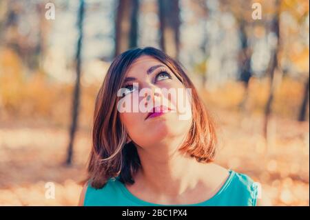 une jolie jeune fille à poil rouge en vêtements bleus regarde dans le parc d'automne Banque D'Images