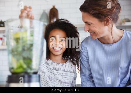 La mère et la fille font un smoothie vert sain dans le mixeur dans la cuisine Banque D'Images