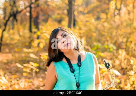 jeune fille saxophoniste à poil noir qui pose sur fond de feuilles jaunes d'un parc d'automne Banque D'Images