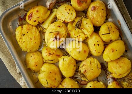 Pommes de terre entières écrasées et croustillantes cuites au four avec assaisonnement et herbes dans un plateau métallique Banque D'Images