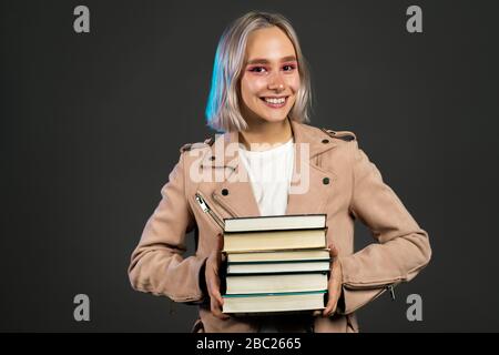 Une jolie étudiante en gris en studio possède une pile de livres universitaires Banque D'Images