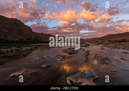 Un beau paysage d'un coucher de soleil doré sur les montagnes et les eaux calmes de la rivière Orange, avec des nuages jaunes spectaculaires reflétant dans l'eau Banque D'Images