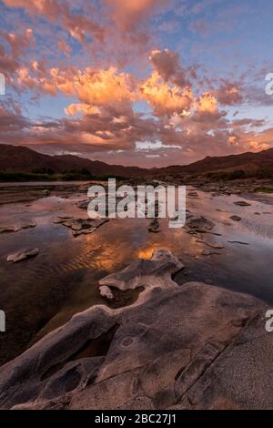 Un paysage vertical d'un coucher de soleil doré sur les montagnes et les eaux calmes de la rivière Orange, avec des nuages orange spectaculaires reflétant dans l'eau Banque D'Images