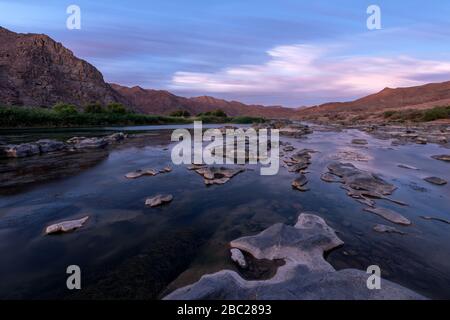 Un beau paysage de longue exposition pris après le coucher du soleil avec les montagnes et la rivière Orange, avec des nuages mouvants spectaculaires reflétant dans le surf de l'eau Banque D'Images