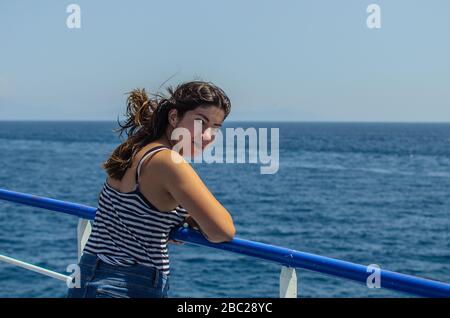 belle jeune fille avec des cheveux sombres dans un t-shirt rayé et des jeans se tient sur le pont d'un bateau en mer Banque D'Images