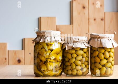 Olives fermentées et artichauts conservés dans de l'huile d'olive dans des bocaux en verre coupés sur fond de bois. Conserve de légumes d'automne Banque D'Images