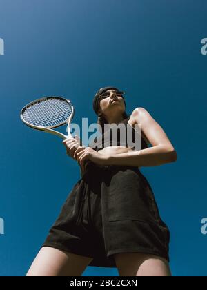 Joueur de tennis photo vue de dessous avec espace copie Girl in black sportswear tient une raquette de tennis sur fond bleu ciel Banque D'Images