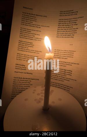 Bougie d'église avec une flamme brûlante photographiée pendant un concert de service carol de Noël. Les mots des chants sont visibles sur la feuille d'hymne derrière. Angleterre Royaume-Uni (116) Banque D'Images