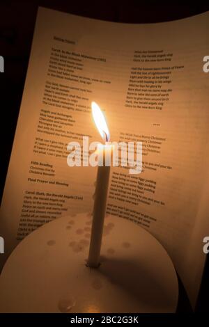 Bougie d'église avec une flamme brûlante photographiée pendant un concert de service carol de Noël. Les mots des chants sont visibles sur la feuille d'hymne derrière. Angleterre Royaume-Uni (116) Banque D'Images