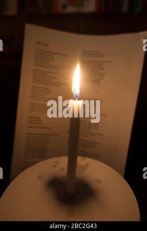 Bougie d'église avec une flamme brûlante photographiée pendant un concert de service carol de Noël. Les mots des chants sont visibles sur la feuille d'hymne derrière. Angleterre Royaume-Uni (116) Banque D'Images