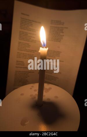 Bougie d'église avec une flamme brûlante photographiée pendant un concert de service carol de Noël. Les mots des chants sont visibles sur la feuille d'hymne derrière. Angleterre Royaume-Uni (116) Banque D'Images