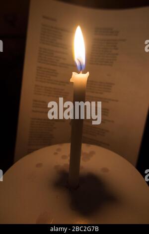 Bougie d'église avec une flamme brûlante photographiée pendant un concert de service carol de Noël. Les mots des chants sont visibles sur la feuille d'hymne derrière. Angleterre Royaume-Uni (116) Banque D'Images