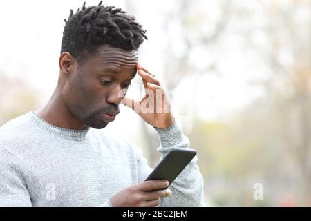 Homme noir se plaignant après avoir fait erreur sur un smartphone debout dans un parc Banque D'Images