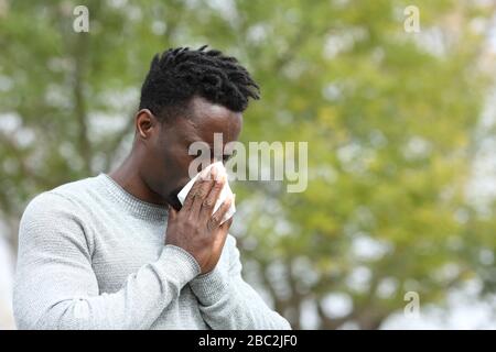 Homme noir allergique soufflant sur l'essuyage dans un parc au printemps saison un jour ensoleillé Banque D'Images
