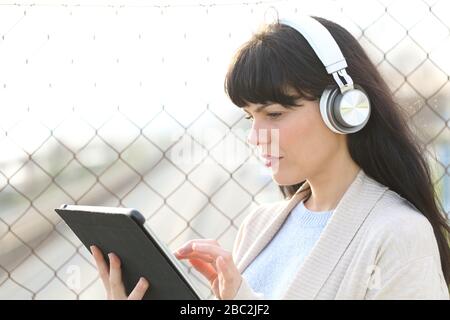 Femme adulte e-learning regarder des médias sur une tablette portant des écouteurs debout dans la rue Banque D'Images