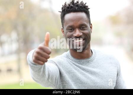 Vue avant portrait d'un homme noir heureux gestuelle pouces vers l'extérieur dans un parc Banque D'Images