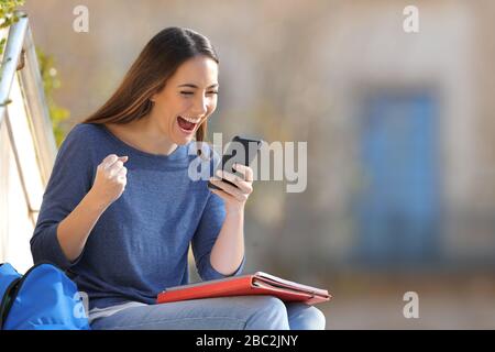 Les étudiants enthousiastes vérifient le contenu d'un smartphone assis à l'extérieur dans un campus universitaire Banque D'Images