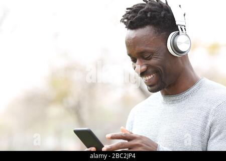 Un homme noir heureux qui écoute de la musique en train de contrôler son smartphone à l'extérieur Banque D'Images