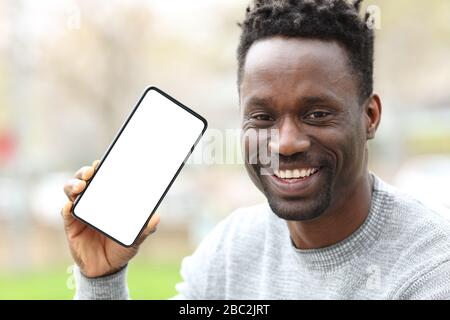 Vue avant portrait d'un homme noir heureux montrant un smartphone avec écran vide dans le parc Banque D'Images
