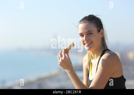 Bonne coureur mangeant la barre de protéines regardant l'appareil photo dans une journée ensoleillée Banque D'Images