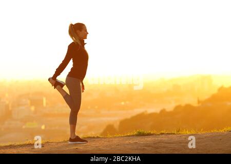 Profil de corps complet d'une femme de coureur qui s'étire seul dans la périphérie de la ville au coucher du soleil Banque D'Images