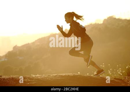 Vue latérale portraif d'une femme de coureur qui monte rapidement un mountaing au coucher du soleil Banque D'Images