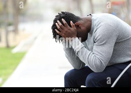 Vue latérale portrait d'un triste homme noir déprimé assis sur un banc dans un parc Banque D'Images