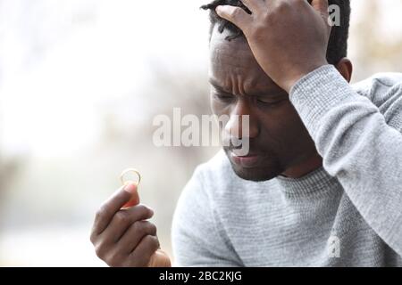 Triste homme noir se plaignant de regarder l'anneau de mariage à l'extérieur dans un parc Banque D'Images