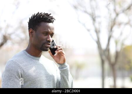 Homme noir sérieux appelant sur un smartphone debout dans le parc Banque D'Images