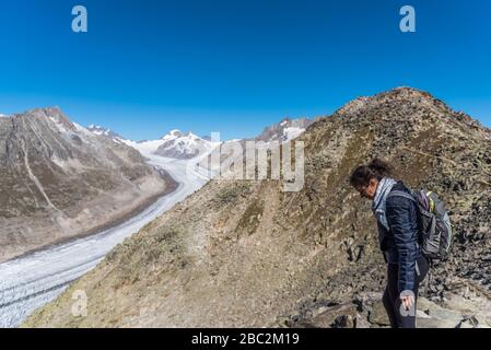 Jeune femme caucasienne avec un sac à dos sur son dos regardant vers le glacier monumental d'Aletsch.ce grand ruisseau de glace, qui s'étend sur 23 km Banque D'Images