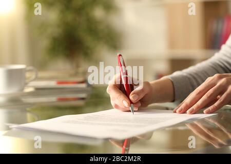Gros plan sur le document de signature des mains d'une femme avec un stylo sur un bureau à la maison Banque D'Images