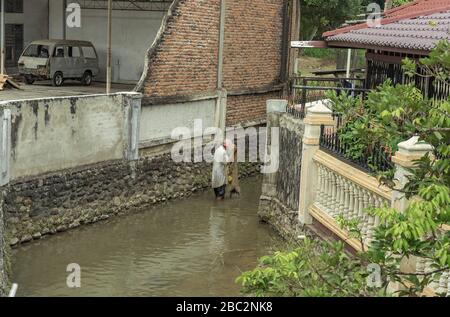21 juin 2018 Panyambungan, Sumatra, Indonésie: Local pauvre pêche avec filet dans la rivière sale et sombre au milieu de la ville aussi vieille voiture sale de shabby visible Banque D'Images