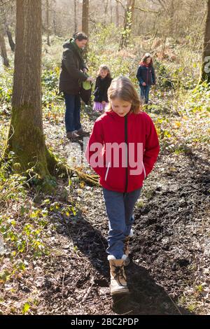 Fille tête mère de 3 enfants trois filles enfants marchant / marchez le long de la voie verdoyante et boueuse / dans la boue sur la voie de la promenade de bois sentier de pied. West End Common, près d'Esher à Surrey, Royaume-Uni. (116) Banque D'Images