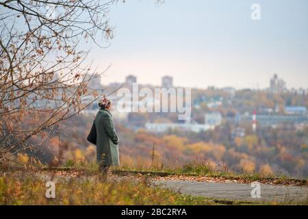 Vieille veuve marchant dans le parc de la ville d'automne. Femme solitaire regardant profondément la ville, l'auto-réflexion. Grand-mère rêvant de son concept familial. Banque D'Images