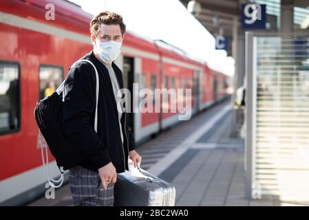 Homme avec une valise sur la plate-forme, il a un masque de visage et des gants contre l'infection avec le virus corona Banque D'Images