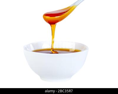 le miel s'écoule de la cuillère en céramique à la cuvette en céramique Banque D'Images