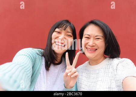 Mère et fille asiatiques prenant selfie avec smartphone mobile en plein air - famille chinoise heureuse ayant plaisir à partager des photos en ligne pour les médias sociaux Banque D'Images