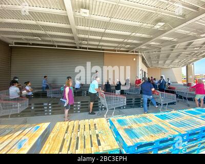 Les acheteurs se font la queue chez Costco pour maintenir la distance sociale. Des palettes en bois ont été placées pour aider les gens à se séparer et à former une ligne avec assez d'espace entre eux. Banque D'Images