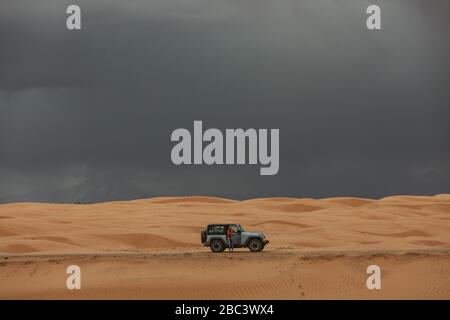 femme et sa jeep en conduisant à travers les dunes de sable sous les cieux orageux Banque D'Images