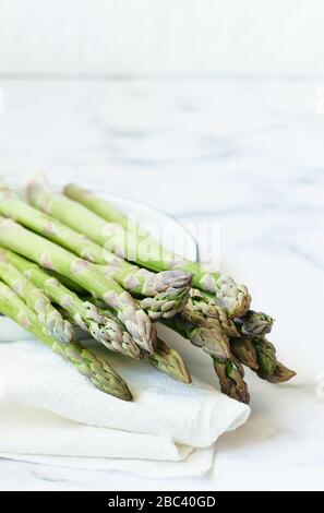 Une bande d'asperges vertes fraîches sur une plaque sur fond de marbre blanc. Concept de mode de vie sain. Banque D'Images