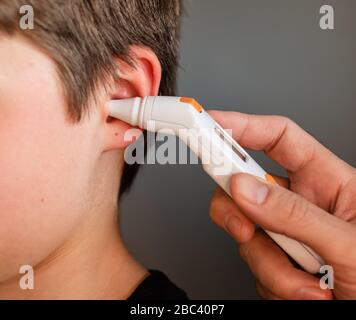 Gros plan de l'enfant qui obtient la température prise avec un thermomètre auriculaire. Banque D'Images